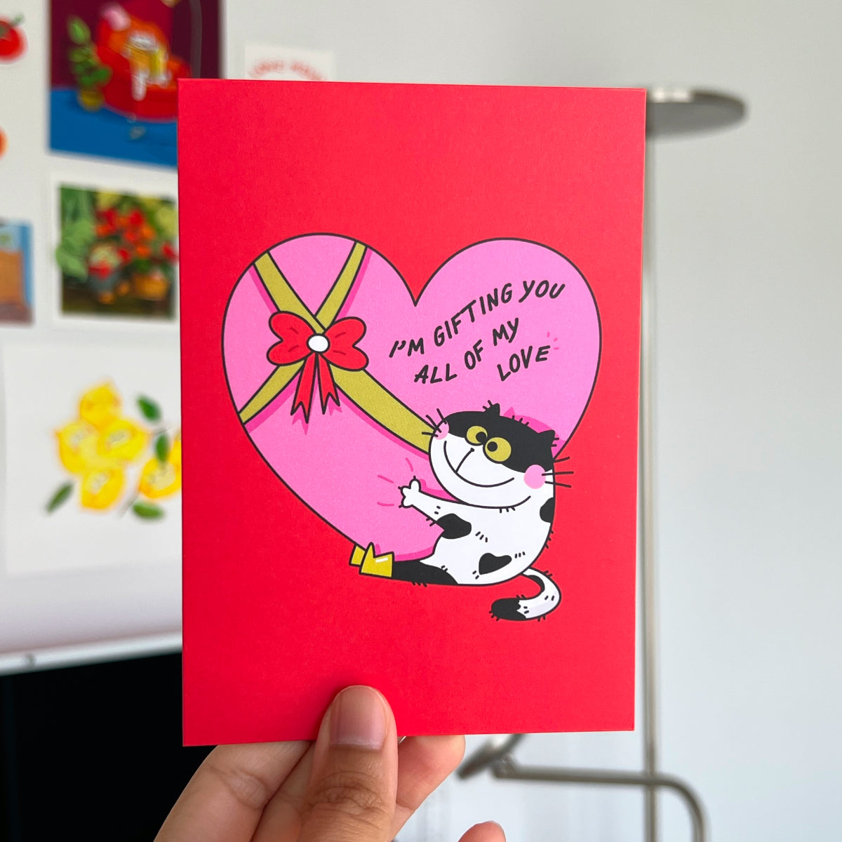 Card with a cat and heart design held by a hand, with a colorful background.