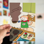 Cartoon character in a kitchen holding a frying pan with text, held by a hand against a blurred background.