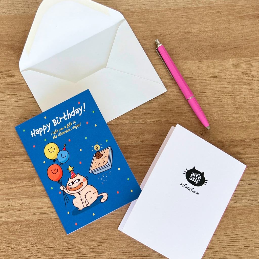 Birthday card with cartoon cat, envelope, and pen on a wooden surface