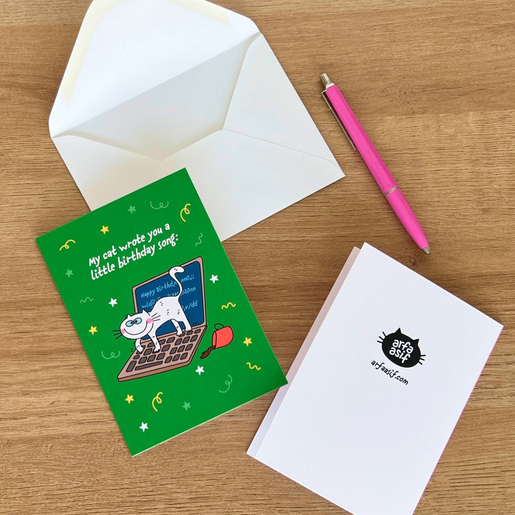 Greeting card with cat illustration, envelope, and pen on a wooden surface