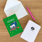 Greeting card with cat illustration, envelope, and pen on a wooden surface