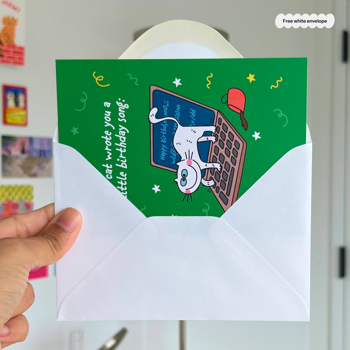 Hand holding a green birthday card with a cat illustration and envelope.