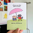 Card with cartoon cats under a pink umbrella and humorous text.