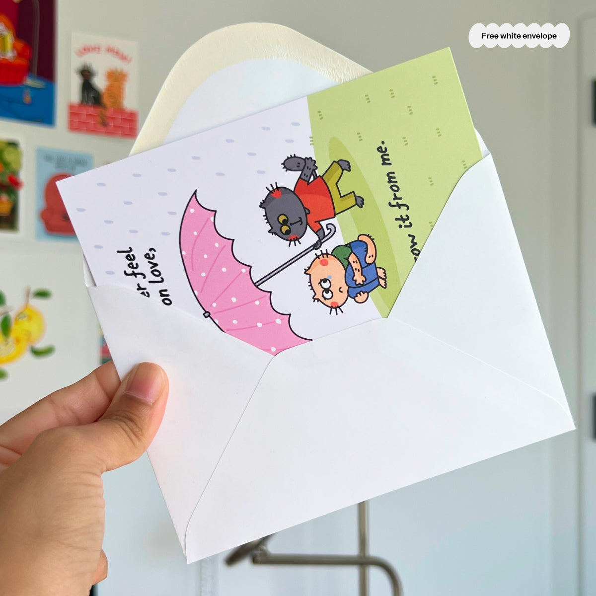 Hand holding a card with cat characters and an envelope on a light blue background