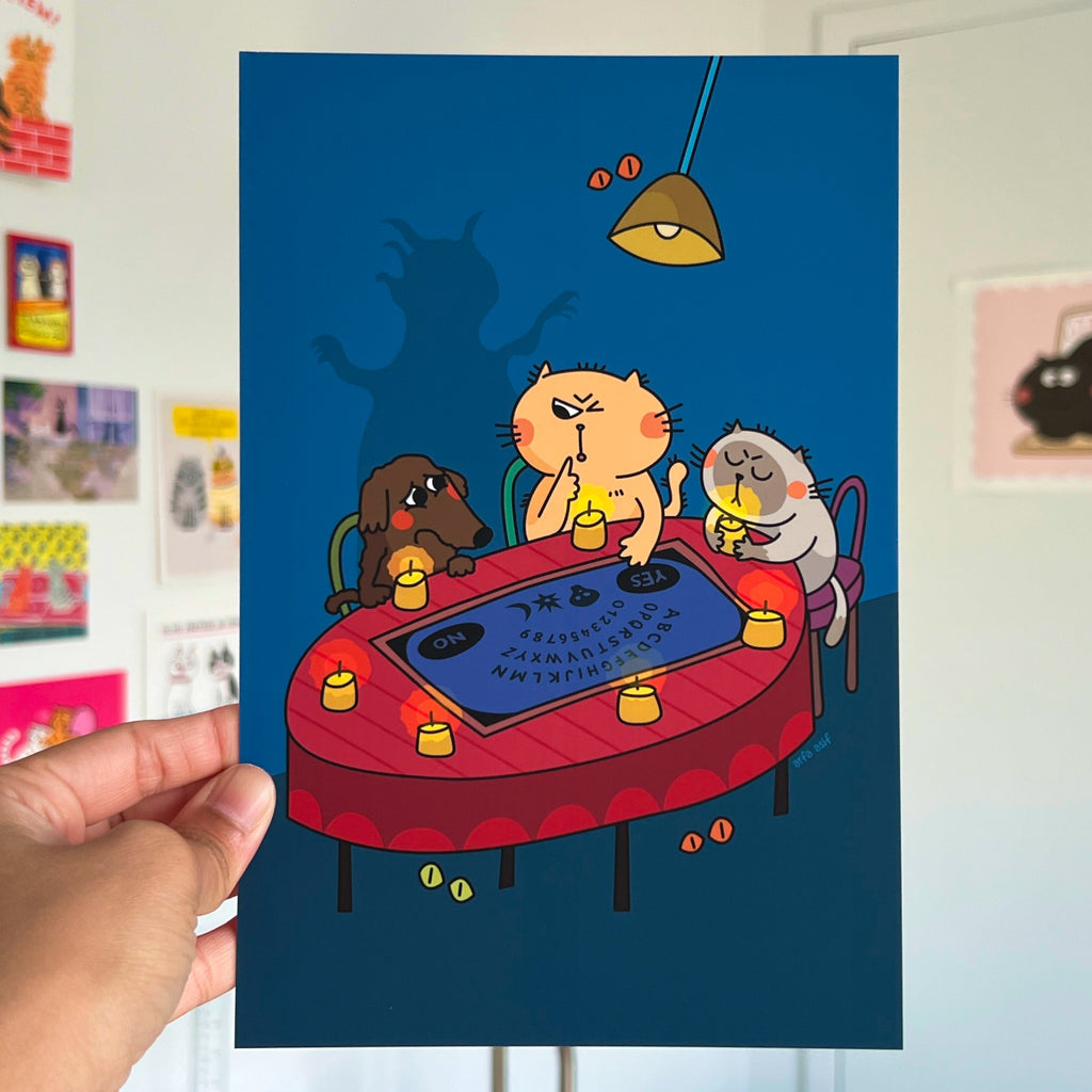 Cartoon cats playing with Ouija Board on a table with a hand holding the poster.