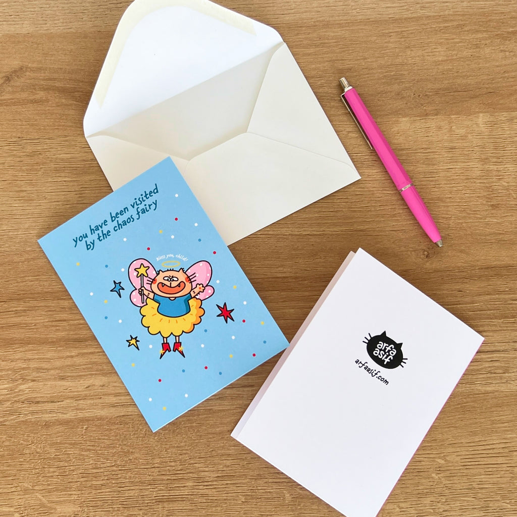 Greeting card with cartoon cat illustration on a wooden surface with an envelope and pen.