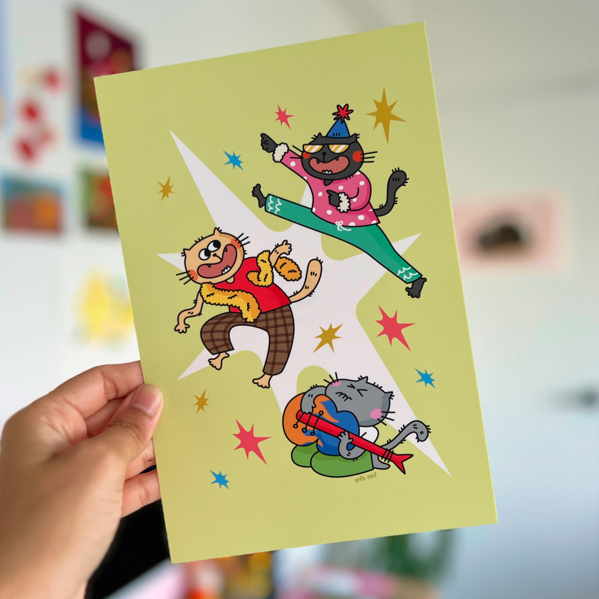 Hand holding a colorful illustration of cartoon characters on a yellow card.