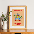 Framed cartoon cat print with a character and text on a wooden shelf with a plant.