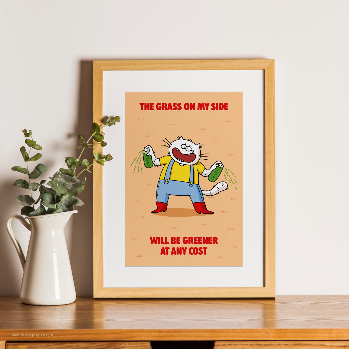 Framed cartoon cat print with a character and text on a wooden shelf with a plant.