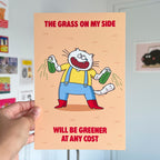 Art print with a cat character holding grass and text on an orange background, held by a hand.