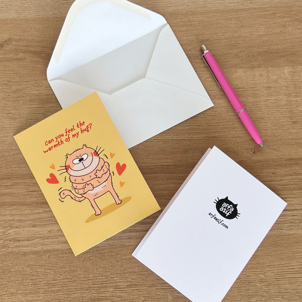Greeting card with cat and envelope on a wooden surface with a pen.