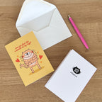 Greeting card with cat and envelope on a wooden surface with a pen.