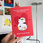 Red card with a cat illustration and text held by a hand, with a blurred background