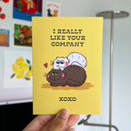 Yellow card with cartoon cats and 'I really like your company' text held in front of a colorful background.
