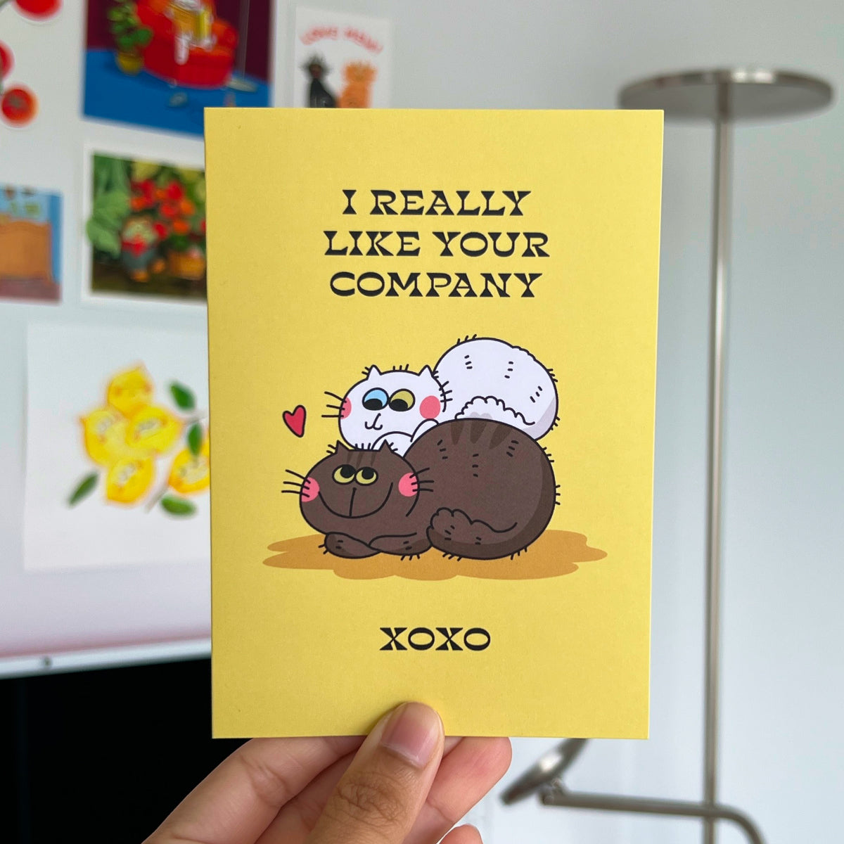Yellow card with cartoon cats and 'I really like your company' text held in front of a colorful background.