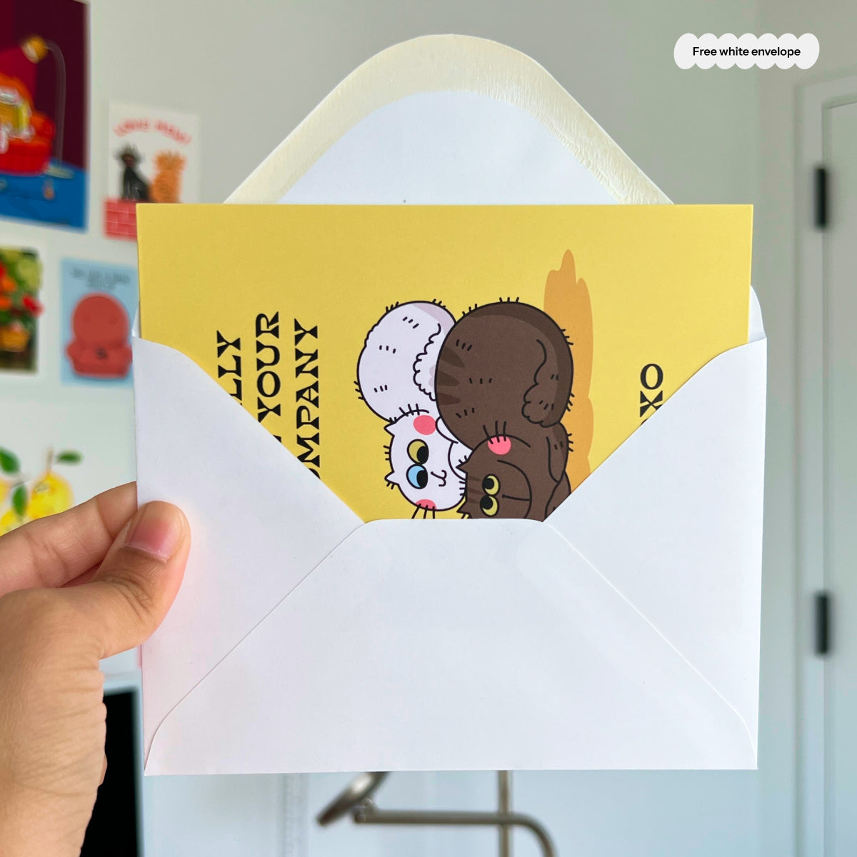 Hand holding a card with cartoon characters and text, inside a white envelope.