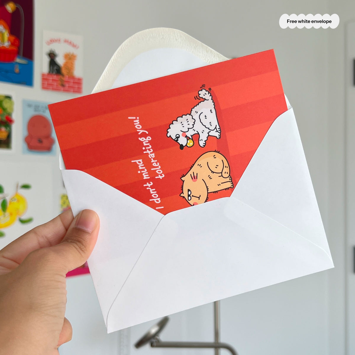 Red card with cartoon cat and dog, and a white envelope held by a hand, with a white envelope.