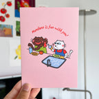 Pink card with cartoon characters and text 'Mundane is fun with you!' held in front of a blurred background.