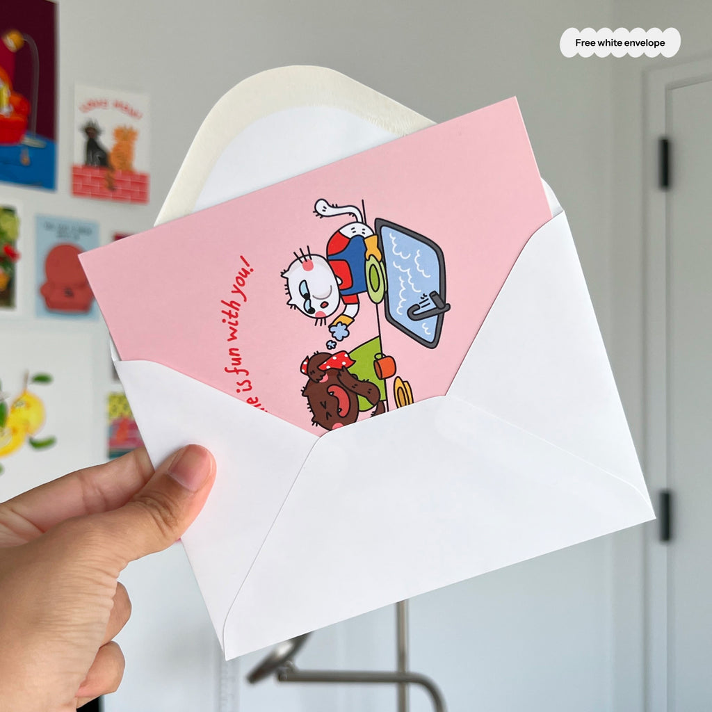 Hand holding a card with a cat character and text, featuring a free white envelope.