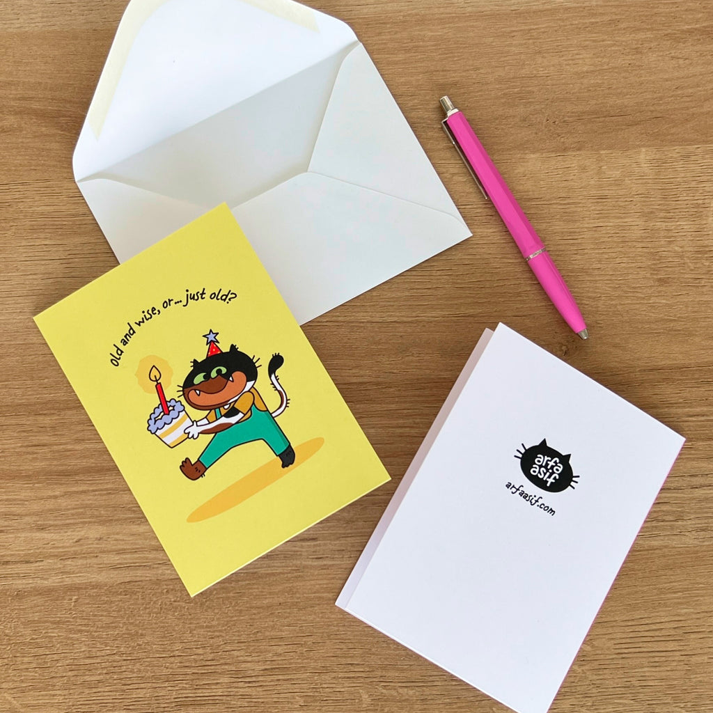 Greeting card with cat character, envelope, and pen on a wooden surface