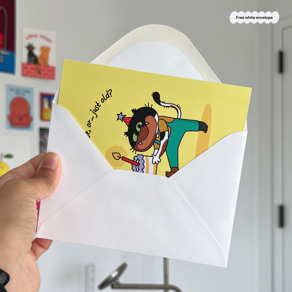 Hand holding a card with a cat character and text, inside a white envelope.