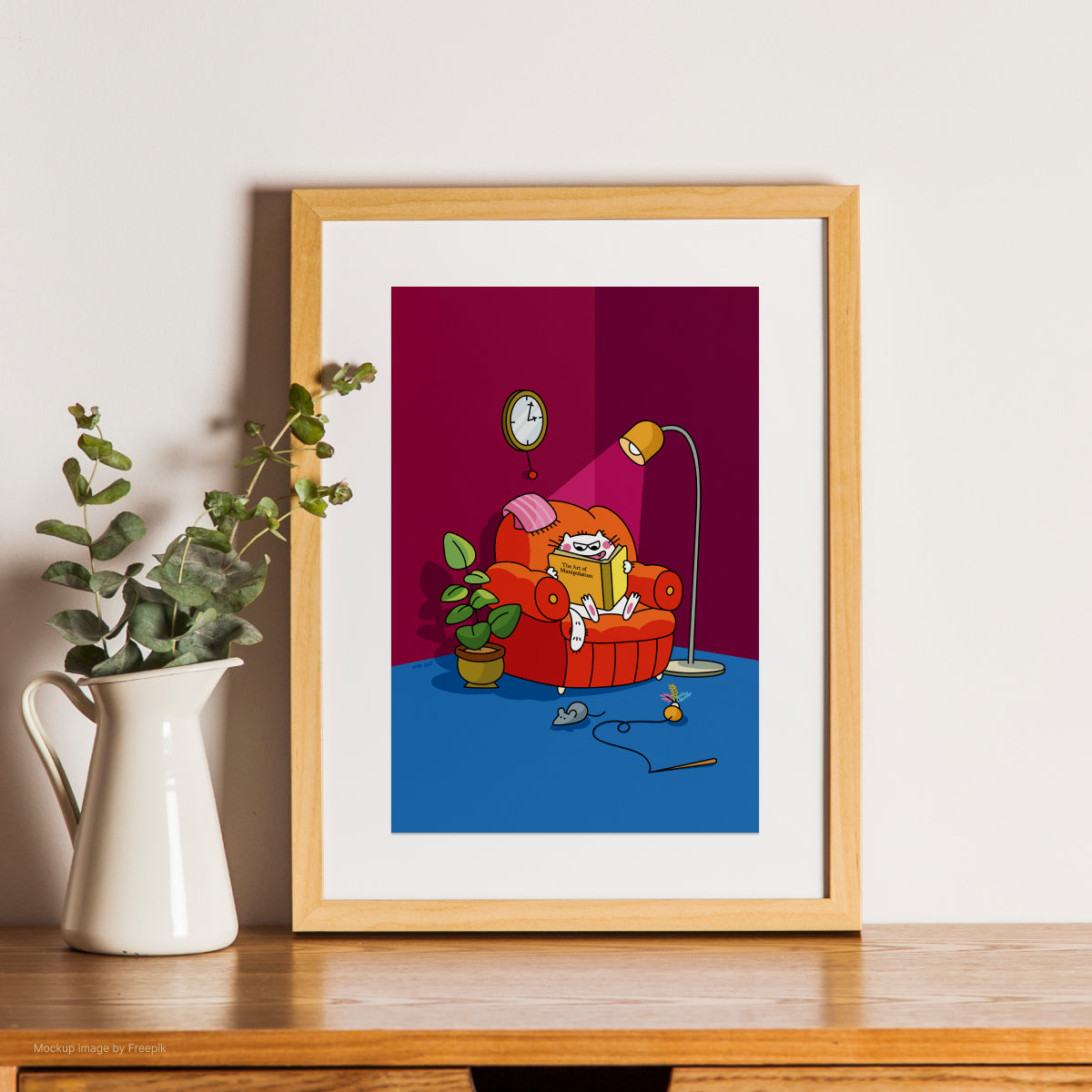 Framed artwork of a cat on an armchair with a plant and clock on a wooden surface.