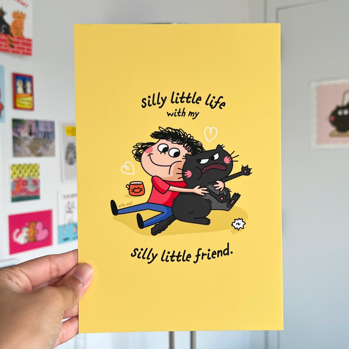 Cartoon illustration of a girl hugging a cat with text on a yellow background, held by a hand.