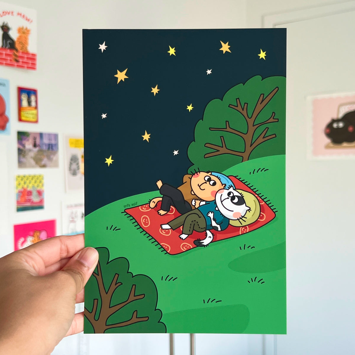 Hand holding a poster with a cartoon of two cats under stars