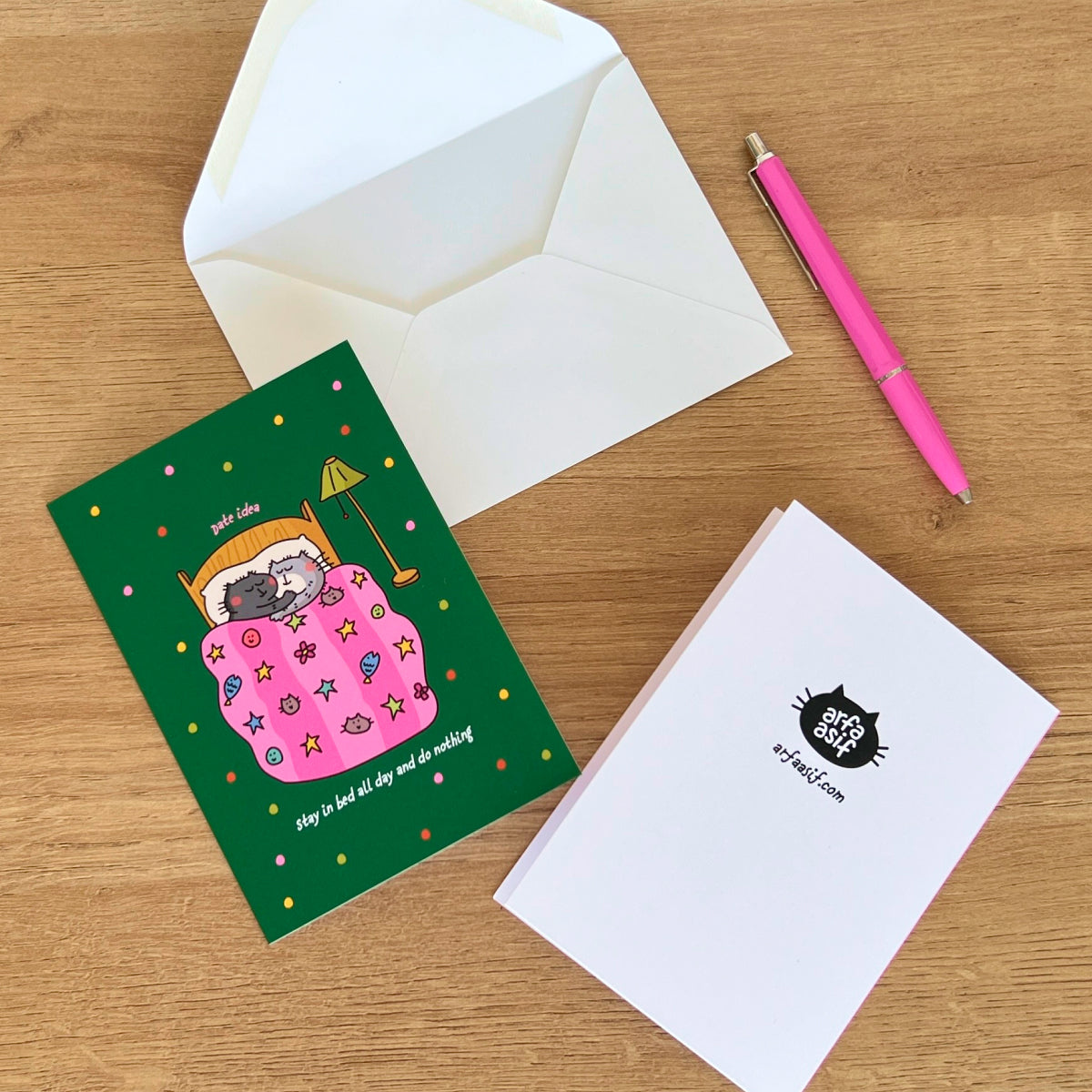 Greeting card with cartoon cat design, envelope, and pen on a wooden surface