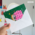 Hand holding a card with a cat illustration and a white envelope.