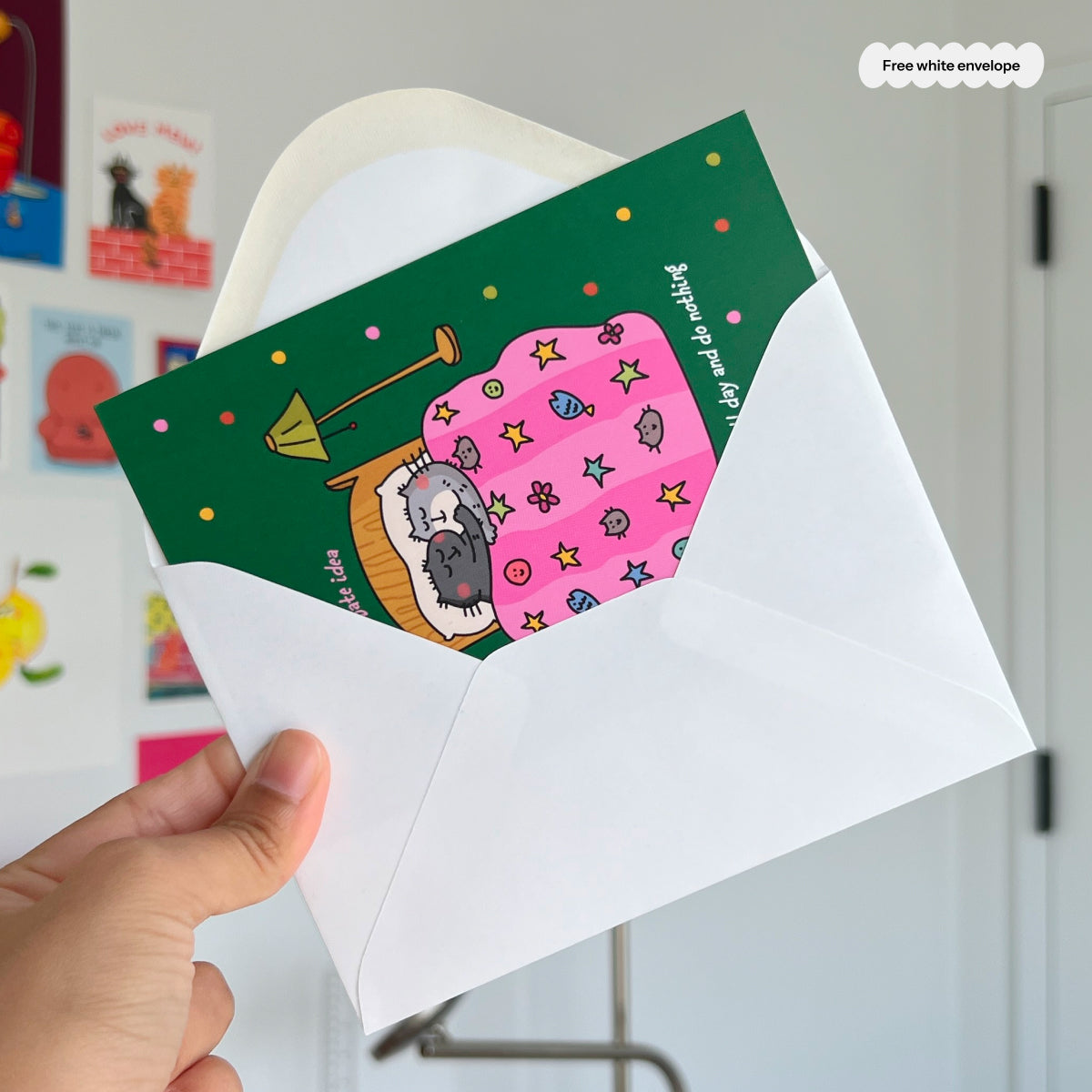 Hand holding a card with a cat illustration and a white envelope.