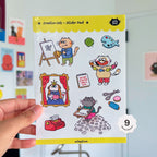 Sticker pack with cat characters held by a hand against a light background