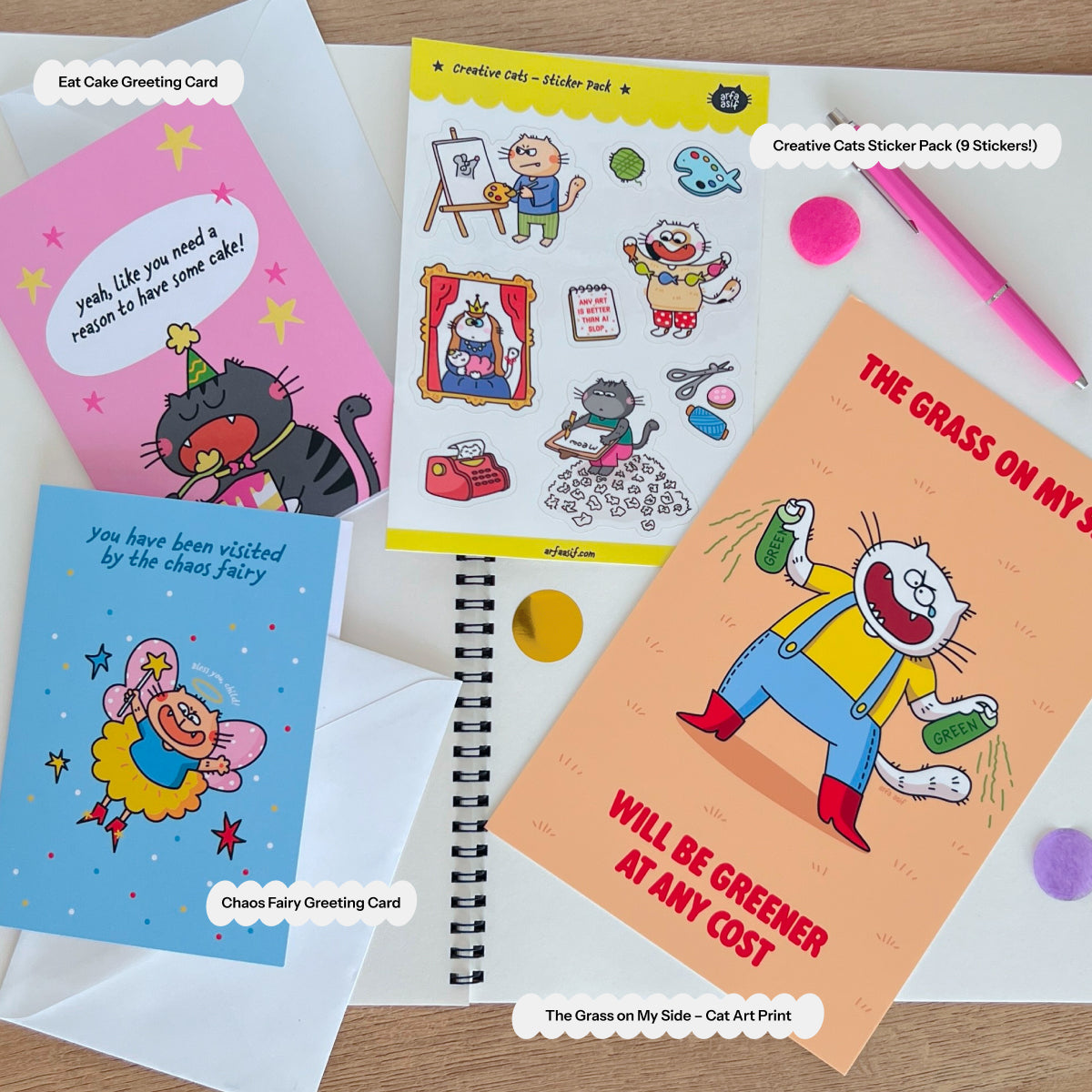 Cat-themed greeting cards, sticker pack, and art print on a wooden surface.