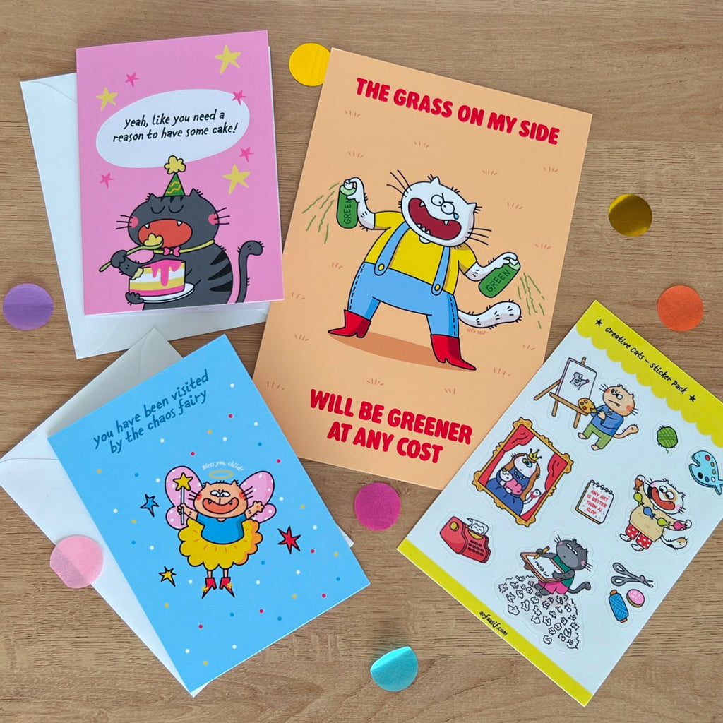 One art print, two colorful greeting cards and a sticker sheet on a wooden surface with decorative confetti.
