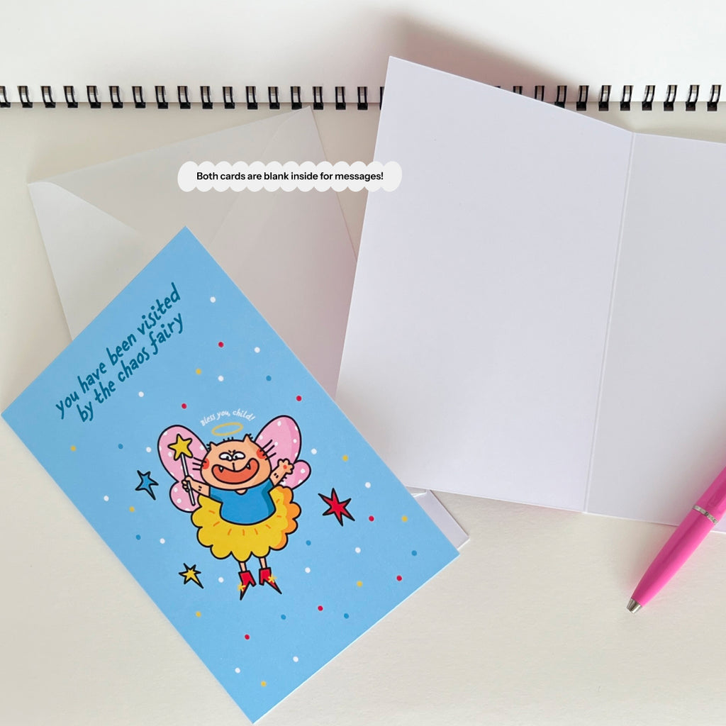 Greeting card with funny cat fairy design on a white surface with an envelope and pen.