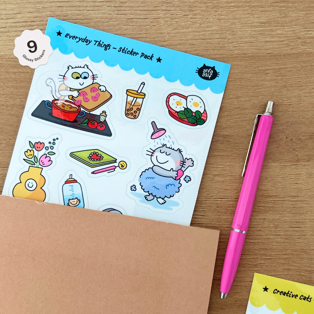 Sticker pack with cartoon cat illustrations on a wooden surface with a pink pen.