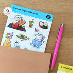 Sticker pack with cartoon cat illustrations on a wooden surface with a pink pen.