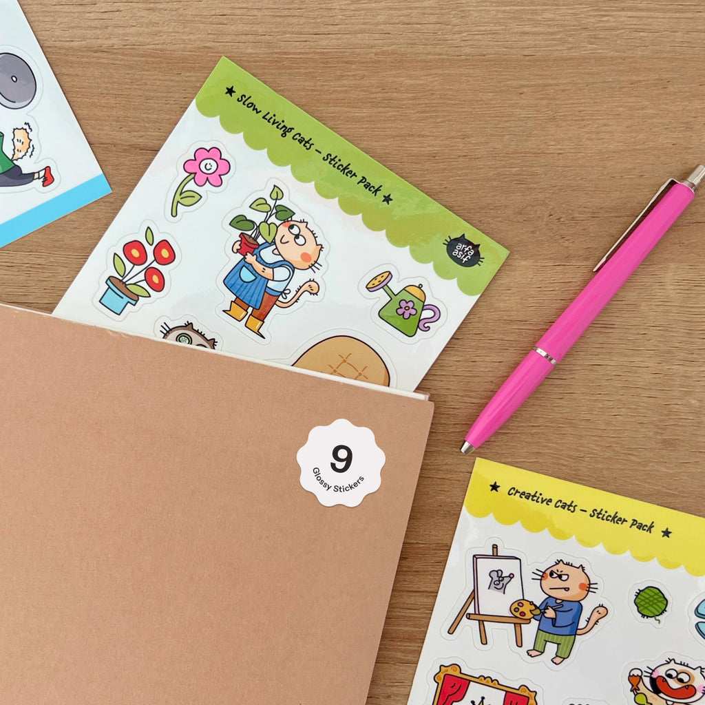 Cat-themed sticker packs on a wooden surface with a pink pen.
